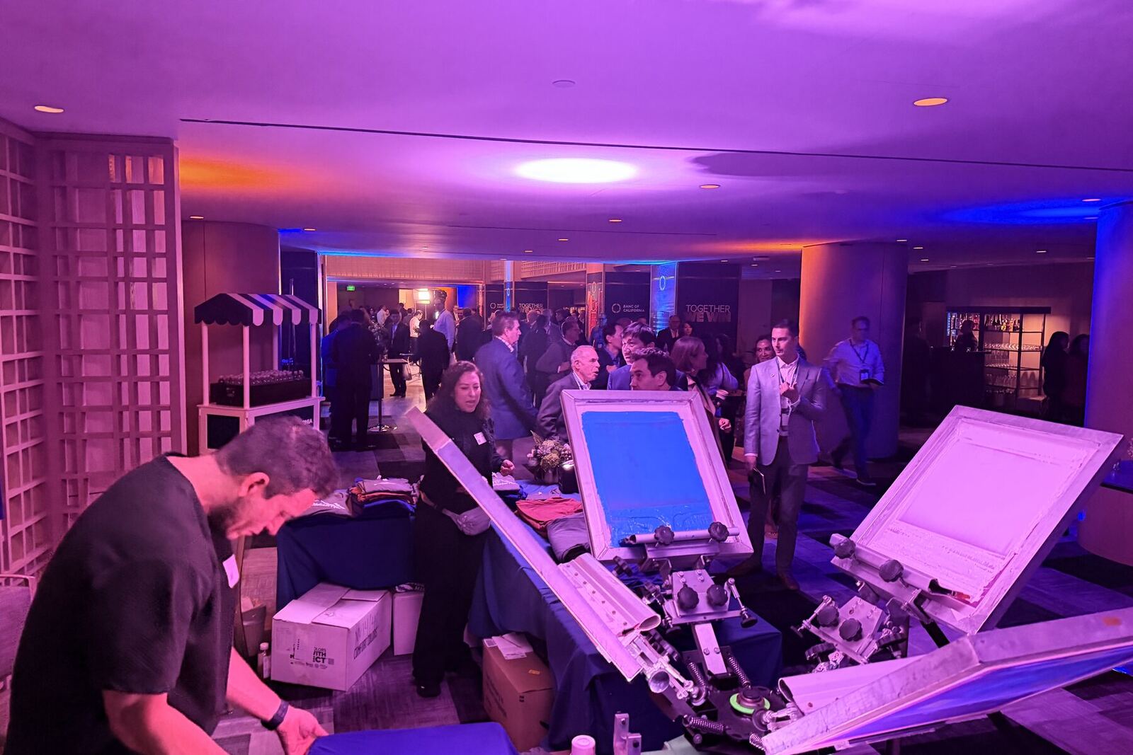 Guests in evening wear gathered around a live customization station under purple uplighting